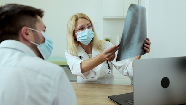 Arts arts in medisch masker specialist die röntgenfoto's van de longen toont aan de patiënt die symptomen verklaart die werken in een modern privéziekenhuis.