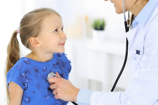 Arts die een klein meisje onderzoekt met een stethoscoop. Gelukkig lachend kind patiënt bij gebruikelijke medische inspectie. Geneeskunde en gezondheidszorg concepten.