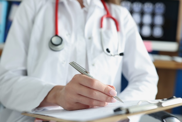 Arts die in medische documenten op klembord in kliniekclose-up schrijft