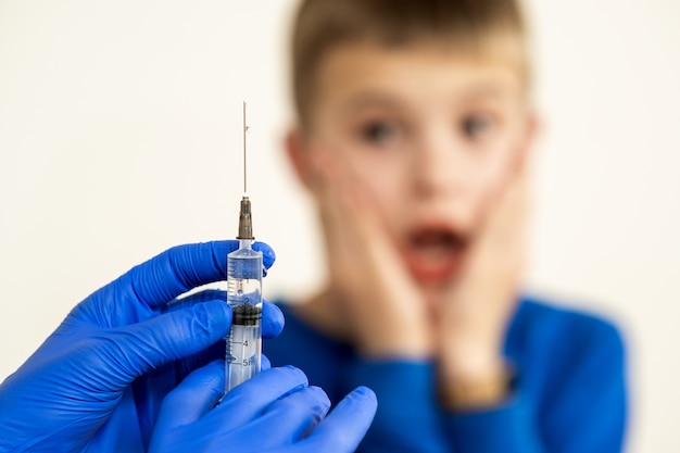 Arts die inentingsinjectie met een spuit voorbereidt op een bange kindjongen. Vaccinatie van kinderen op school concept.