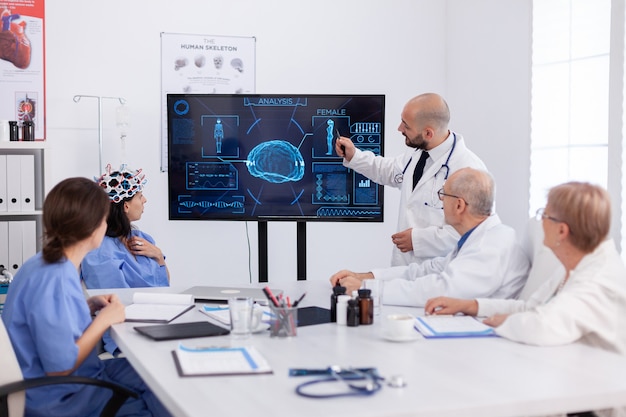 Arts die medische radiografie wijst naar ziekenhuismedewerkers die de presentatie van hersenziekte analyseren met behulp van hightech in de vergaderruimte