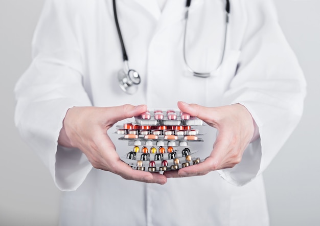 Arts die stapel verschillende pillen, antibiotica en virusbehandelingstabletten op grijze het ziekenhuismuur houdt.