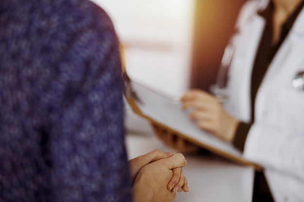 Arts en patiënt bespreken huidig gezondheidsonderzoek terwijl ze in een zonnige kliniek zitten. Perfecte medische service in het ziekenhuis.