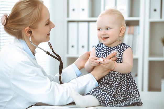 Arts en patiënt in het ziekenhuis. Klein meisje gekleed in donkerblauwe jurk in erwten wordt onderzocht door een arts met een stethoscoop. Geneeskunde concept.
