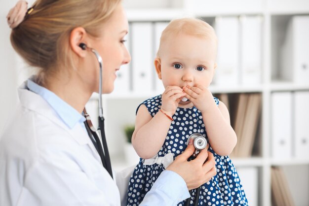 Arts en patiënt in het ziekenhuis. klein meisje gekleed in donkerblauwe jurk wordt onderzocht door arts met een stethoscoop. geneeskunde en gezondheidszorg concept.