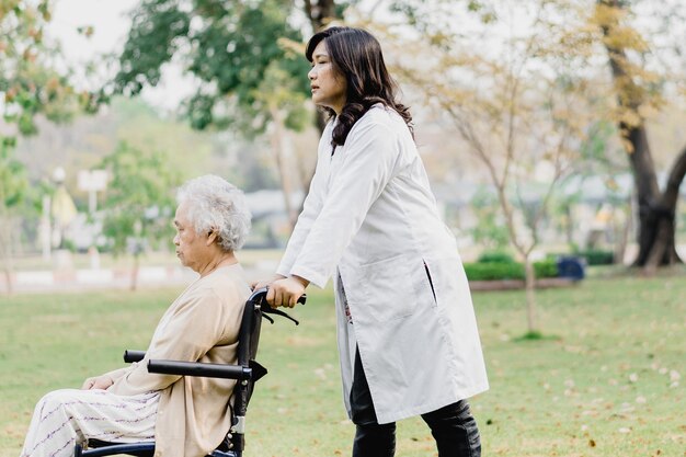 Arts helpt en geeft Aziatische senior vrouw patiënt zittend op een rolstoel in het park