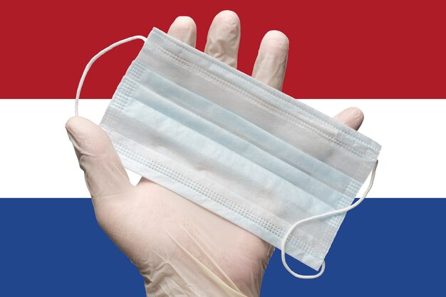 arts houdt gezichtsmasker in de hand in witte medische handschoen op achtergrondvlag van nederland concept