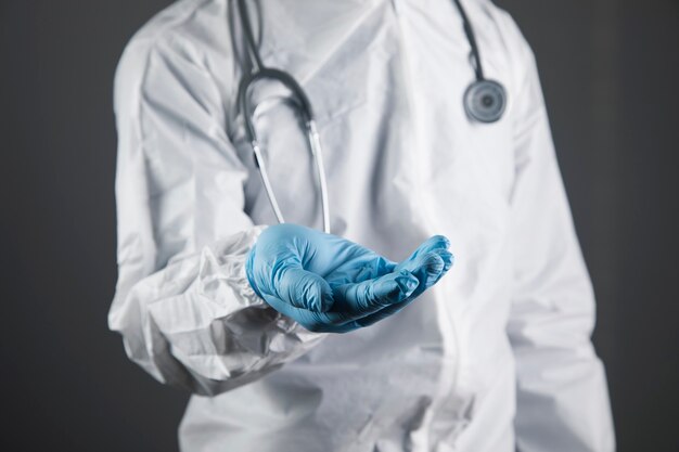 Arts in beschermend uniform toont open handpalmen. handen in de vorm van een standaard op een grijze scène