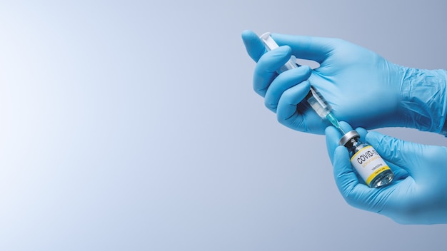 Arts in blauwe latexhandschoenen vult spuit in met vaccin uit glazen flesje