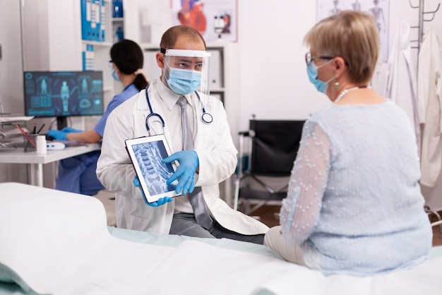 Arts in de gezondheidszorg die gezichtsmasker draagt als veiligheidsmaatregel die röntgenfoto's op tablet-pc toont in de tijd van covid19