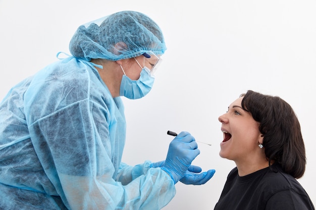 Arts in een beschermend pak die een keel- en neusuitstrijkje van een patiënt neemt om te testen op mogelijk