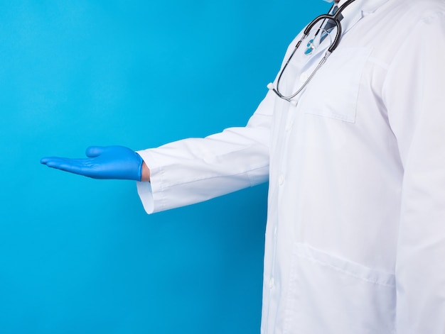 Arts in een witte jas, blauwe latex handschoenen en een beschermend masker op zijn gezicht houdt voorwaardelijk een voorwerp vast