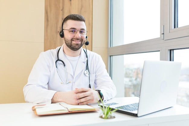 Arts in witte medische jas en hoofdtelefoon teleconferentie op laptop maken