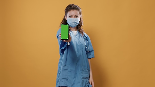Arts met een stethoscoop die smartphone vasthoudt en sms't met een groen schermmodel op de camera. Dokter in ziekenhuisuniform met chirurgisch masker met touchscreen-apparaat dat kopieerruimte presenteert.