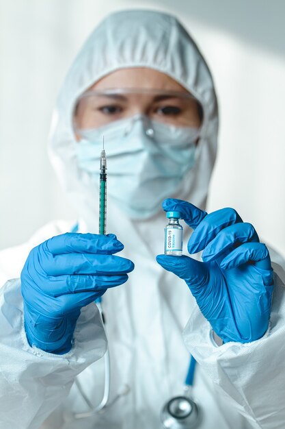 Arts of verpleegkundige in een beschermend pak houdt een spuit en een covid 19-vaccin vast
