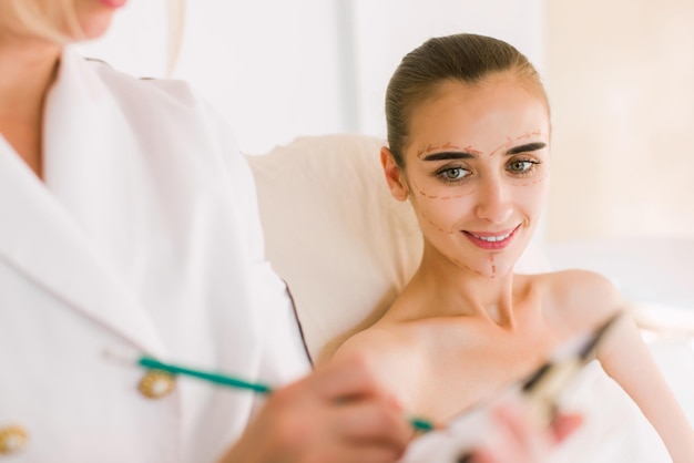 Arts of verpleegkundige in gesprek met de patiënt in de cosmetologiekliniek. Correctielijnen op het gezicht van de vrouw.