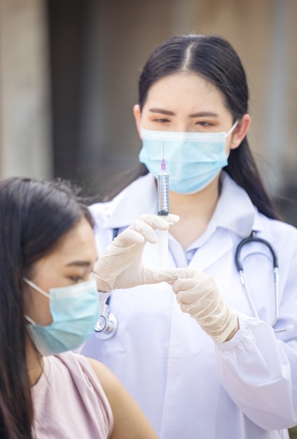 Arts of verpleegkundige in het openluchtziekenhuis met een spuit met vloeibare vaccins die zich voorbereiden om een injectie te doen. Medische apparatuur. Mensen in wit uniform, gewaad.