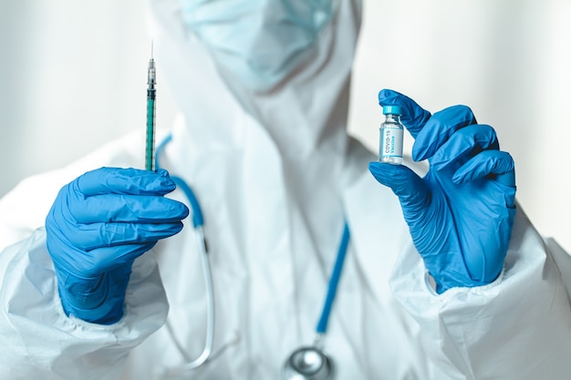 Arts of verpleegster in een beschermend pak houdt een spuit en covid 19-vaccin vast