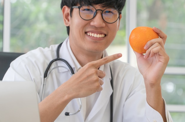 Arts of voedingsdeskundige houdt oranje en richt uw vinger op de sinaasappel en glimlacht in de kliniek.