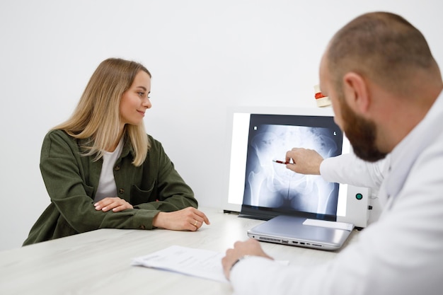 Arts-orthopedist die röntgenfoto toont aan zijn vrouwelijke patiënt tijdens consultatie in de kliniek