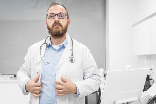 Arts van middelbare leeftijd met een witte medische jas in de kliniek met serieuze uitdrukking