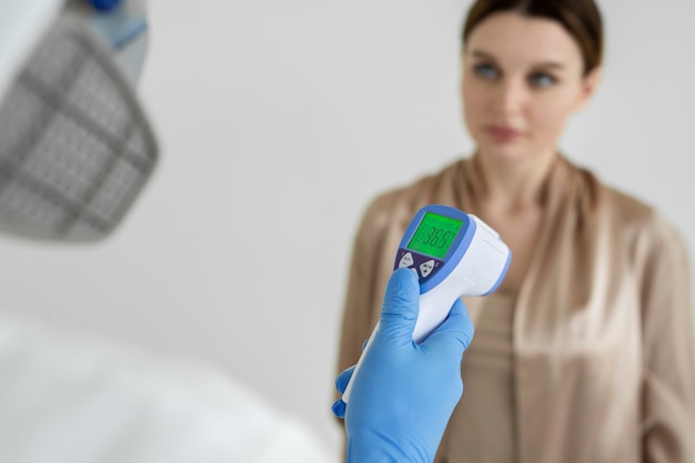 Arts voor infectieziekten meet de temperatuur van een vrouwelijke patiënt met een infraroodthermometer in een kliniek tijdens de coronavirusepidemie. Covid-19