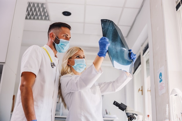 Artsen met gezichtsmaskers en rubberen handschoenen die röntgenfoto van de longen bekijken.