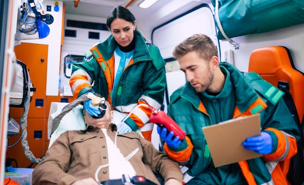 Artsen noodhulp of paramedici werken met een senior man patiënt terwijl hij op een brancard in een ambulance ligt.