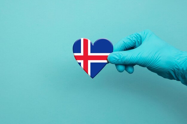 Artsenhand die chirurgische handschoen dragen die het hart van de vlag van IJsland houden