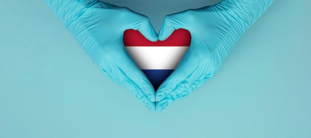 Artsenhanden die blauwe chirurgische handschoenen dragen die het vormsymbool met de vlag van nederland horen