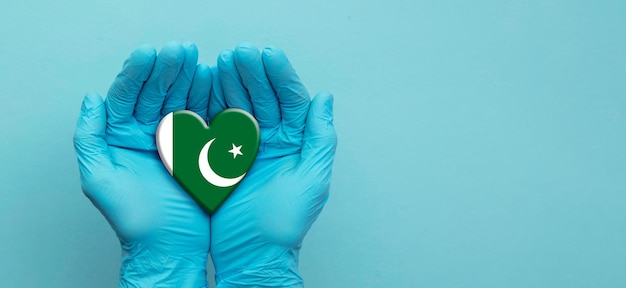 Artsenhanden die chirurgische handschoenen dragen die het hart van de vlag van Pakistan vasthouden