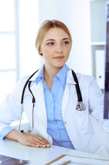 Artsenvrouw die röntgenfoto onderzoekt dichtbij venster in het ziekenhuis. Chirurg of orthopedist op het werk. Geneeskunde en gezondheidszorgconcept. Blauw gekleurde blouse van een therapeut ziet er goed uit.