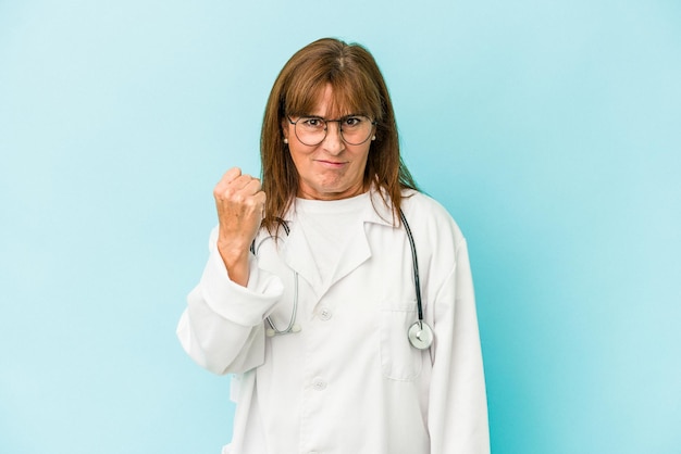 Artsenvrouw van middelbare leeftijd die op roze achtergrond wordt geïsoleerd die vuist toont aan camera, agressieve gezichtsuitdrukking.