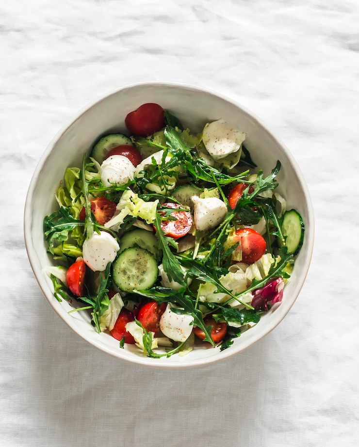 Photo arugula cherry tomatoes cucumbers mozzarella cheese salad with lemonmustard dressing on a light background top view