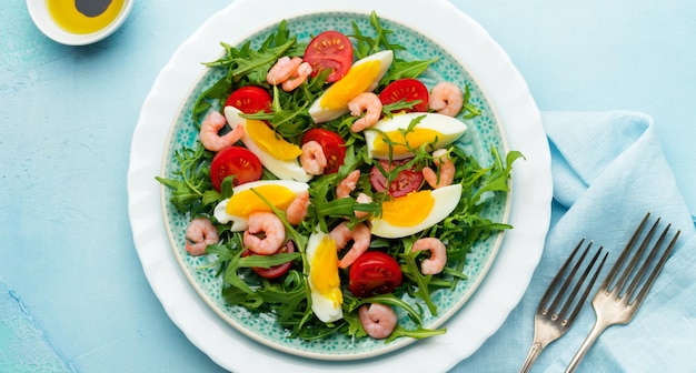 Insalata di rucola, cetriolo, pomodoro, uova e gamberetti con salsa di soia su piatto di ceramica. messa a fuoco selettiva. vista dall'alto.