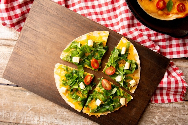 Arugula handgemaakte pizza geserveerd in een houten snijplank boven een houten tafel met een rode picknickdoek