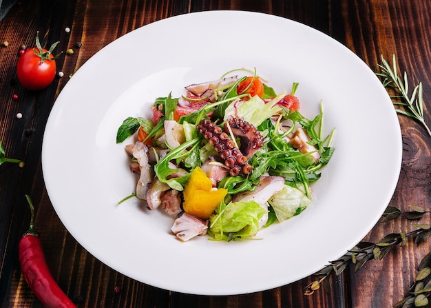 Салат из рукколы с осьминогом на белой тарелке