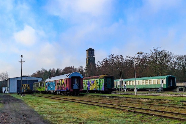 2023년 12월 17일 림부르크 벨기에(Limburg Belgium)는 기차역의 사용되지 않는 선로에 있는 낡은 객차와 맑은 가을날 푸른 하늘을 배경으로 한 전망대를 배경으로 하고 있습니다.
