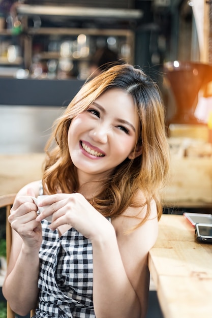 asain schoonheid meisje gelukkig in checker jurk lachend met warme koffie in coffeeshop