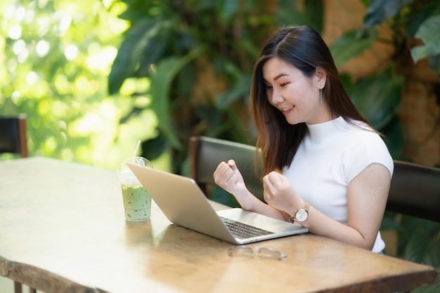 Asain women happy and successfully working with laptop on the table in the cafe