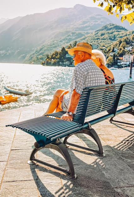 아스코나, 스위스 - 2016년 8월 23일: 여름에 스위스 티치노 주의 마조레 호수에 있는 아스코나 고급 관광 리조트의 벤치에 앉아 있는 낭만적인 노부부. 사람들이 야외 거리 여행.
