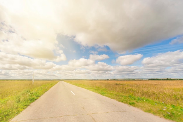 Asfaltweg door het veld met groen gras onder blauwe lucht met wolken