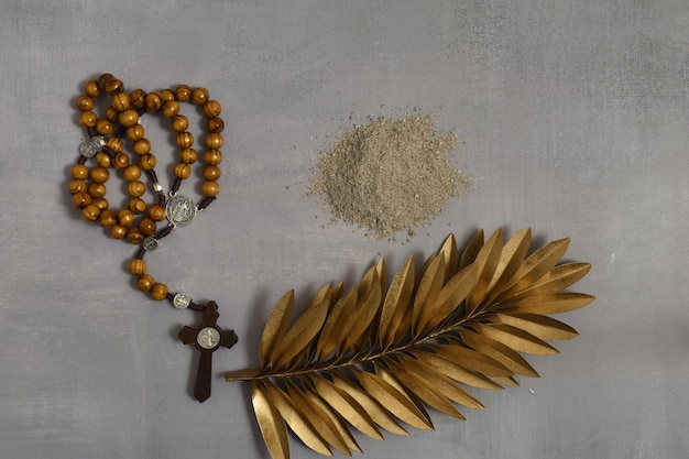 Ash rosary and golden palm leaf on grey backgroun Ash Wednesday concept