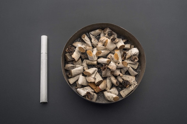 Ashtray with cigarette butts against the background of a gray table. A new cigarette is near.