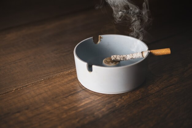 Ashtray with cigarette on wood table.