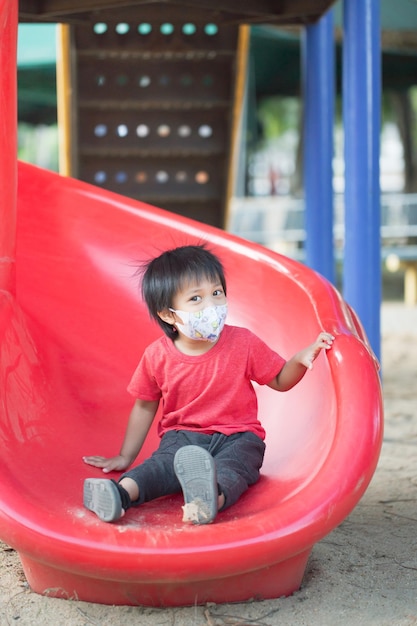 Asia child smiling playing on slider bar toy outdoor playground\
happy preschool little kid having funny while playing on the\
playground equipment in the daytime in summer