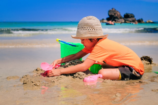 Un ragazzo carino asiatico che gioca la sabbia da solo sulla spiaggia.