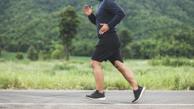 산을 배경으로 도로를 달리는 운동복을 입은 아시아 남자. 자연 속에서 운동을 위해 조깅하는 젊은 남자. 건강한 생활 방식과 스포츠 개념