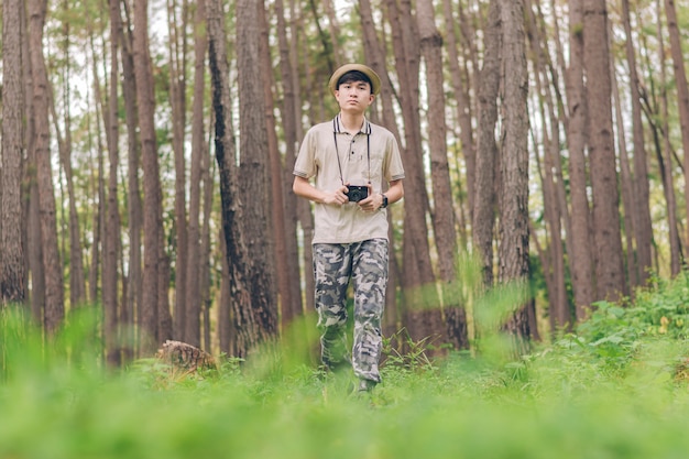 아시아 남자 셔츠, 모자를 착용하고 위장 바지는 걷고 숲에서 사진을 찍고있다
