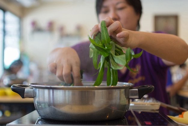 野菜を鍋に入れて調理するアジア人女性